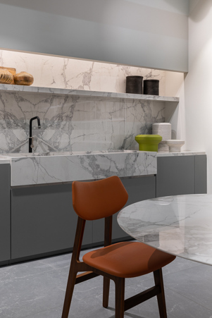 Moderne Küche mit maßgeschnittener Tischplatte, großer Spüle, Arbeitsplatte, Regal und Küchenverkleidung aus Gres Marble White matt in Spiegelbild verlegt.